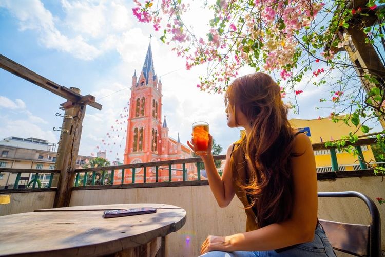 Une vietnamienne dégustant un thé glacé avec en fond l'église de Dinh Tan à Ho Chi Minh, au Vietnam