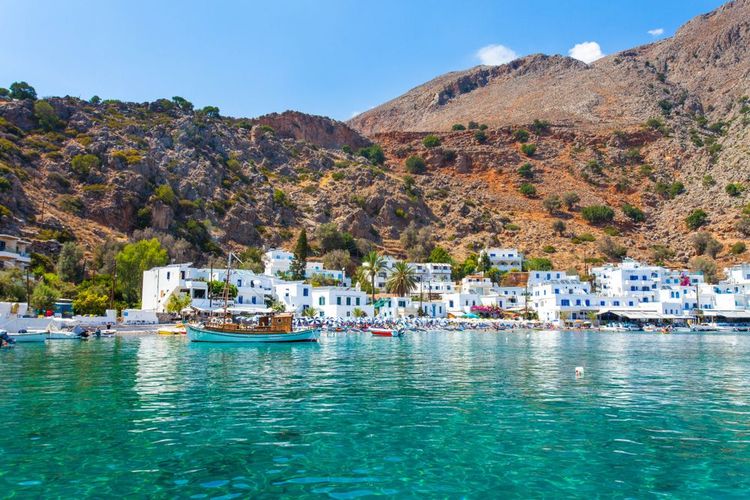 Le village blanc de Loutro, les pieds dans l'eau et l'îlot rocheux derrière.
