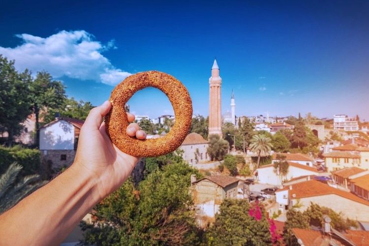 Le bagel turc se présente comme un authentique repas de rue traditionnel à la main sur fond de la vieille ville d'Antalya avec des monuments célèbres comme le minaret Yivli.