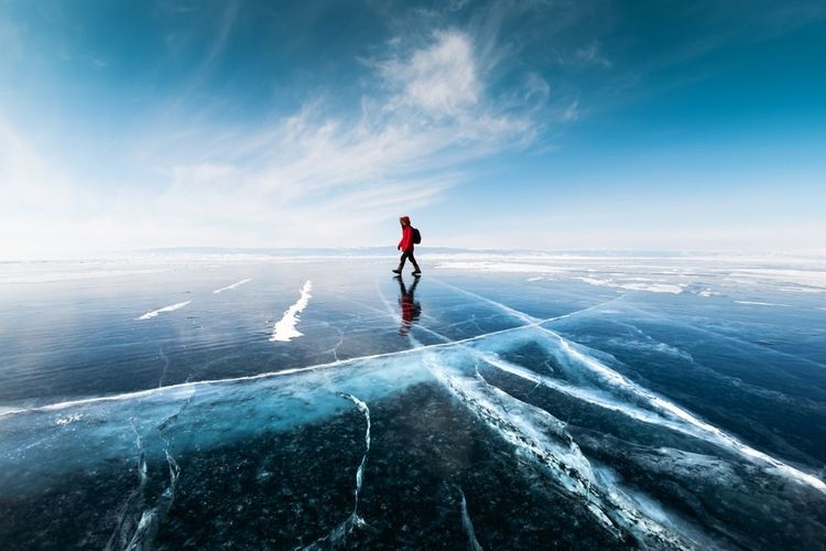 Homme touriste marchant sur la glace du lac Baikal. Paysage hivernal du lac Baikal, Sibérie, Russie. Bleu transparent craquelé de glace et ciel bleu