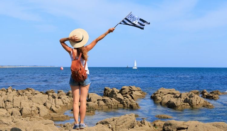 Une femme tenant le drapeau breton sur une plage de l'Atlantique