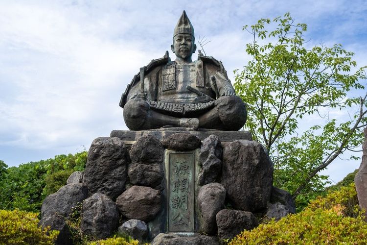 Statue en bronze du shogun Minamoto no Yoritomo assis en armure sur une base en pierre dans le parc Genjiyama, Kamakura, entouré de verdure et de ciel