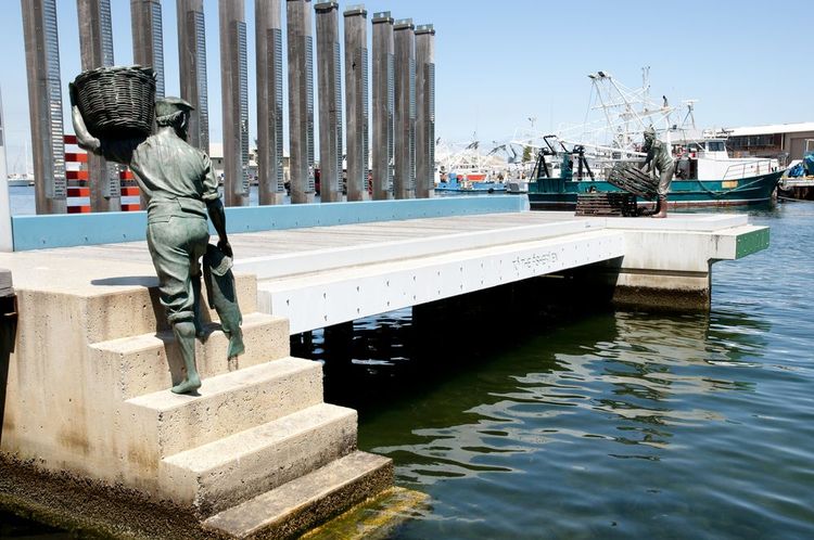 Le "monument aux Pêcheurs" vu dans son intégralité dans le port de Fremantle, avec la statue du pêcheur, de dos, qui monte un panier de poissons